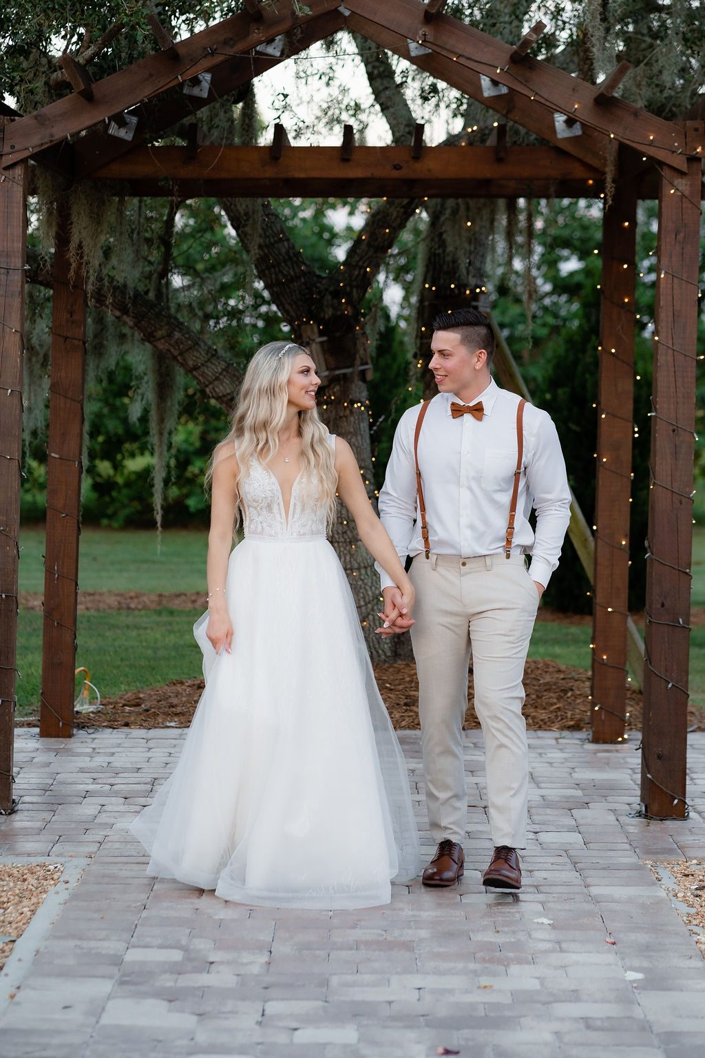 Bride and groom walking under a lit pergola at dusk — captured by Precious Pics Production